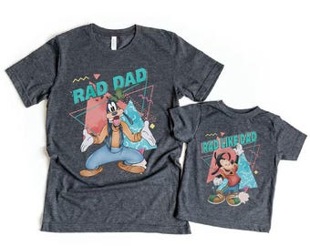 May include: Two dark gray t-shirts with cartoon graphics. The larger shirt says "RAD DAD" with a Goofy character illustration. The smaller shirt says "RAD LIKE DAD" with a Max character illustration. Both shirts have a retro 80s design.