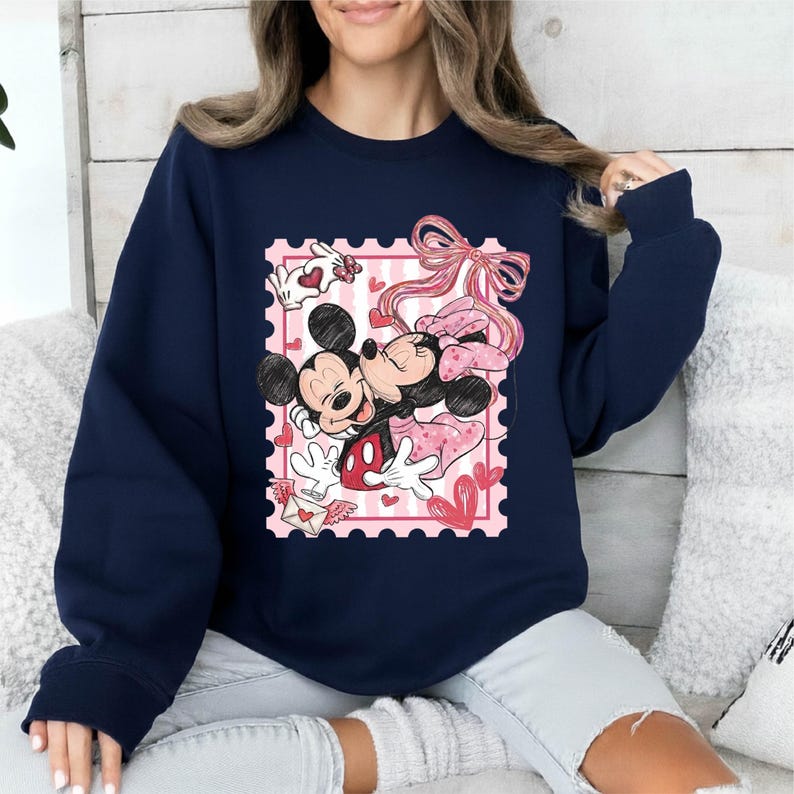 Puede incluir: Sudadera azul marino con un dise&ntilde;o de Mickey y Minnie Mouse abraz&aacute;ndose dentro de un dise&ntilde;o de sello postal rosa. El dise&ntilde;o incluye corazones, lazos y una carta de amor, creando un tema rom&aacute;ntico. La sudadera es una prenda c&oacute;moda e informal.
