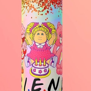 May include: A pink and white tumbler with a glitter design. It features a cartoon image of a Cabbage Patch Kid doll, a Care Bear, and a Strawberry Shortcake doll. The text "FRIENDS" is printed on the tumbler.