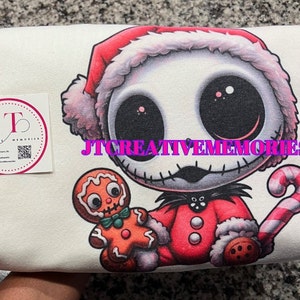 May include: White t-shirt with a cartoon image of Jack Skellington from The Nightmare Before Christmas dressed as Santa Claus. He is holding a gingerbread man and a candy cane. The text "JT CREATIVE MEMORIES" is printed on the shirt.