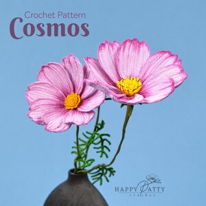 Könnte beinhalten: Häkelmuster für Kosmosblumen. Zwei rosa gehäkelte Kosmosblumen mit gelben Zentren stehen in einer Vase. Der Text "Crochet Pattern Cosmos" befindet sich oben im Bild. Der Text "HAPPY PATTY crochet" befindet sich unten im Bild.