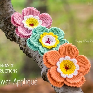 May include: Three crocheted flower appliques in pink, green, and orange. Each flower has a white centre with a yellow circle and a red centre. The flowers are arranged on a branch.