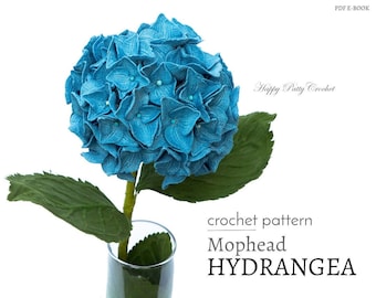 May include: A crochet pattern for a blue mophead hydrangea flower. The pattern is called "Mophead Hydrangea" and is available as a PDF e-book. Happy Patty Crochet.