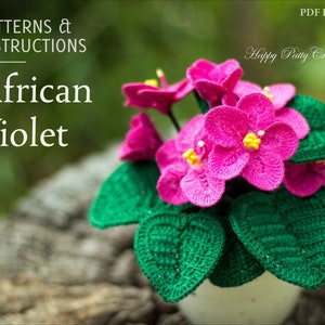 Op de afbeelding: Gehaakte Afrikaanse viooltjesplant met roze bloemen en groene bladeren in een witte pot. Het patroon en de instructies voor dit project zijn beschikbaar als een PDF e-book. Happy Patty Crochet.