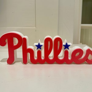 May include: Red and white 3D sign with the word "Phillies" in red and two blue stars.