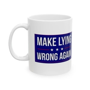 Może przedstawiać: Biały kubek ceramiczny z niebiesko-czerwonym nadrukiem, na którym widnieje napis "MAKE LYING WRONG AGAIN" z trzema gwiazdami.