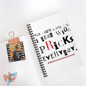 May include: A white spiral-bound notebook with the text "You can't scare me. I deal with pricks everyday." in a ransom note style. A photo is clipped to the notebook with a copper clip.