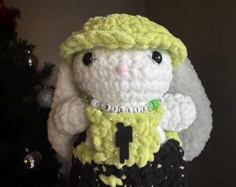 May include: A white crocheted bunny wearing a lime green hat and overalls with a black and lime green pattern. The bunny has a beaded necklace with the word "BILLIE" spelled out in white beads.