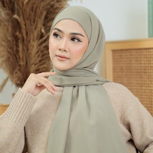 May include: A woman wearing a light green hijab. The hijab is made of a soft, flowing fabric. The woman is wearing a beige sweater.
