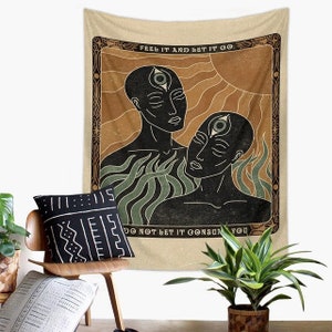 May include: A tapestry with a beige background and a brown frame. The tapestry features a black and white illustration of two people with a third eye. The text "FEEL IT AND LET IT GO. DO NOT LET IT CONSUME YOU" is printed on the tapestry.