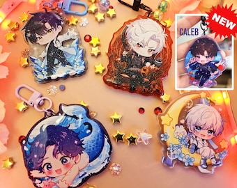 Może przedstawiać: Cztery kolorowe breloki z postaciami anime z błyszczącymi akcentami. Breloki przedstawiają postacie o różnych kolorach włosów i strojach. Breloki znajdują się na białym tle z złotym i srebrnym brokatem.