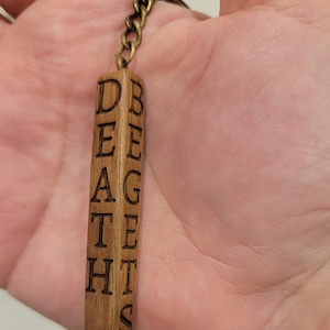 May include: A wooden keychain with the words "Death Gets" and "Begets" engraved on it. The keychain is attached to a bronze chain.