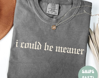 May include: A gray t-shirt with the text "i could be meaner" in a gothic font. The shirt is made of a soft, comfortable material and has a relaxed fit.