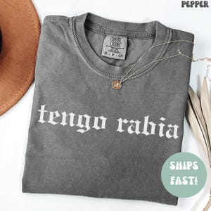 May include: Gray t-shirt with the text "tengo rabia" in white gothic font. The shirt is made of a soft, comfortable material.