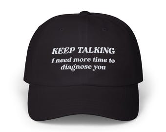 May include: Black baseball cap with white embroidered text that reads "KEEP TALKING I need more time to diagnose you". The cap has a curved brim and a rounded crown. The hat is a classic style.