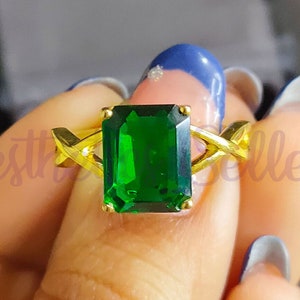 May include: A gold ring with a large emerald green gemstone. The ring has a criss-cross design on the band.