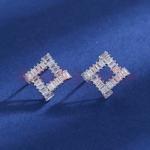 Könnte beinhalten: Ein Paar silberne Ohrringe mit quadratischem Design. Jeder Ohrring besteht aus kleinen, klaren Zirkonia-Steinen, die in einem geometrischen Muster gesetzt sind.