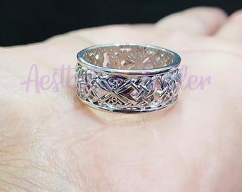 May include: A silver Celtic knot ring with a detailed design. The ring is wide and has a smooth finish.