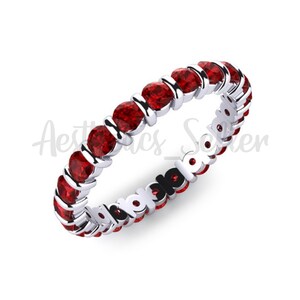 May include: A white gold eternity band with a row of red gemstones.