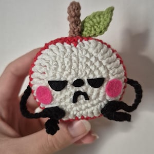 Peut inclure: Pomme crochetée faite à la main avec un visage grincheux. La pomme a un bord rouge, un centre blanc et des yeux et une bouche noirs. Elle a des joues roses, des bras noirs, une tige marron et une feuille verte. Création originale.