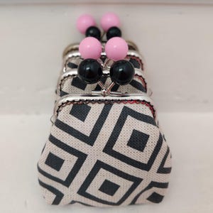 May include: A set of four small coin purses with black and white geometric patterns. Each purse has a black and pink button closure.