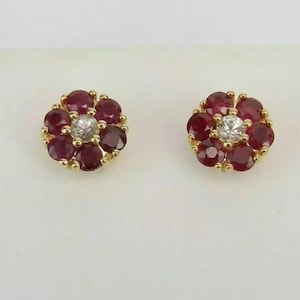 Può includere: Un paio di orecchini d'oro con un design a forma di fiore. Ogni orecchino presenta un gruppo di rubini rossi che circondano un singolo diamante bianco.