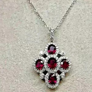 May include: A silver necklace with a pendant featuring a cluster of five red gemstones surrounded by smaller clear gemstones.