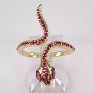 May include: A gold ring shaped like a snake with red ruby stones. The snake is coiled and has a head with two ruby eyes.