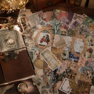 Könnte beinhalten: Ein braunes Lederjournal mit einem Metallanhänger und einer dekorativen Karte auf dem Einband, umgeben von einer Sammlung an Papier-Ephemera im Vintage-Stil, darunter florale Drucke, verzierte Rahmen, Schmetterlingsmotive und kleine Aufkleber.
