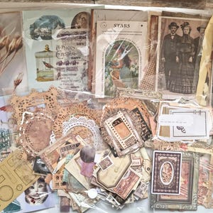 Op de afbeelding: Een verzameling vintage scrapbookpapier, stickers en ephemera. De collectie bevat afbeeldingen van botanische elementen, antieke portretten en architectonische ontwerpen. Het kleurenpalet is voornamelijk sepia, beige en cr&egrave;me.