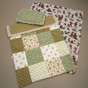 May include: A patchwork quilt, pillow, and blanket set. The quilt features squares of green and white floral and patterned fabrics. The pillow and quilt trim have white lace. A blanket with a repeating pattern of children playing is also included.