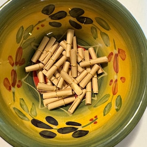 May include: A decorative ceramic bowl with a yellow interior and green rim, filled with small rolled paper scrolls secured with gold wire. The bowl features a floral design with green leaves and orange accents.