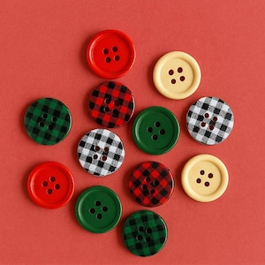 May include: A collection of colorful buttons in various designs. The buttons include solid red, green, and yellow, as well as plaid patterns in red and black, green and black, and black and white. The buttons are arranged on a red background.