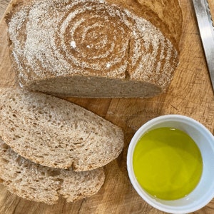 Puede incluir: Un pan reci&eacute;n horneado con un dise&ntilde;o en espiral, cortado para revelar la textura. Dos rebanadas de pan y un peque&ntilde;o cuenco de aceite de oliva est&aacute;n sobre una tabla de madera. Tambi&eacute;n se ve un cuchillo.