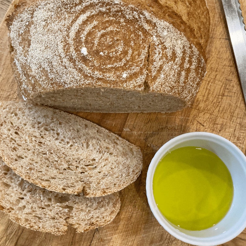 Puede incluir: Un pan reci&eacute;n horneado con un dise&ntilde;o en espiral, cortado para revelar la textura. Dos rebanadas de pan y un peque&ntilde;o cuenco de aceite de oliva est&aacute;n sobre una tabla de madera. Tambi&eacute;n se ve un cuchillo.