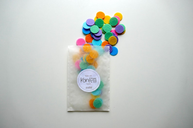 Może przedstawiać: Przezroczysty plastikowy woreczek wypełniony kolorowymi k&oacute;łkami konfetti z filcu w odcieniach niebieskiego, zielonego, ż&oacute;łtego, pomarańczowego i fioletowego. Woreczek ma białą etykietę z napisem "Made with Konfetti regn  pastel".