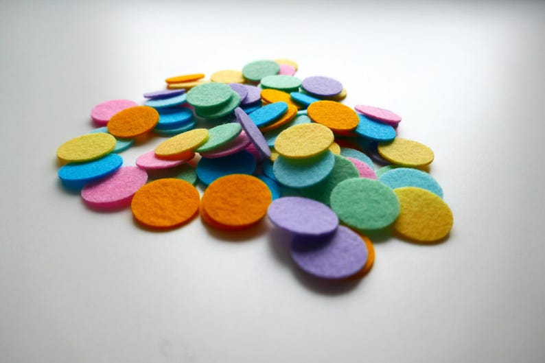 Może przedstawiać: Stosik kolorowych k&oacute;łek z filcu w r&oacute;żnych odcieniach niebieskiego, zielonego, ż&oacute;łtego, pomarańczowego i fioletowego. K&oacute;łka są ułożone w przypadkowy wz&oacute;r i wszystkie są tej samej wielkości.