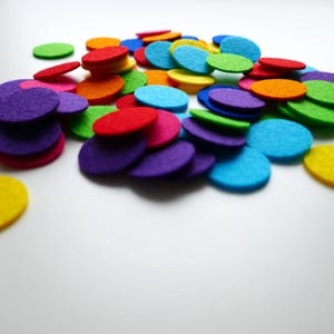 Może przedstawiać: Kolekcja kolorowych k&oacute;łek z filcu w r&oacute;żnych odcieniach czerwieni, pomarańczy, ż&oacute;łci, zieleni, błękitu, fioletu i r&oacute;żu. K&oacute;łka są ułożone w przypadkowy wz&oacute;r na białym tle.