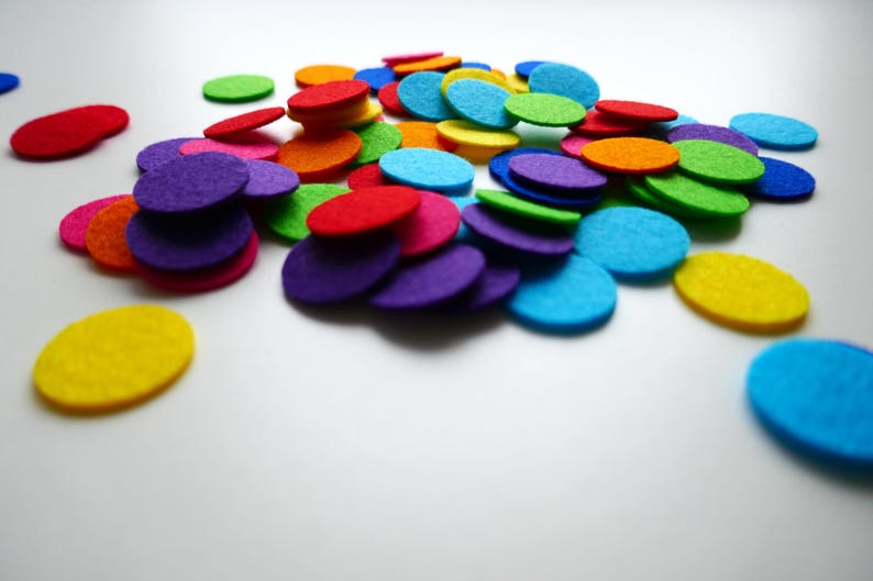 Może przedstawiać: Kolekcja kolorowych k&oacute;łek z filcu w r&oacute;żnych odcieniach czerwieni, pomarańczy, ż&oacute;łci, zieleni, błękitu, fioletu i r&oacute;żu. K&oacute;łka są ułożone w przypadkowy wz&oacute;r na białym tle.