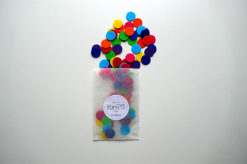 Może przedstawiać: Biała papierowa torebka wypełniona kolorowymi k&oacute;łkami konfetti z filcu. Torebka ma etykietę z napisem "Konfetti" i małym symbolem serca.