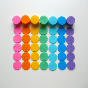 Może przedstawiać: Tęczowe filcowe k&oacute;łka ułożone w rzędach, z kolorami przechodzącymi od r&oacute;żowego do fioletowego.