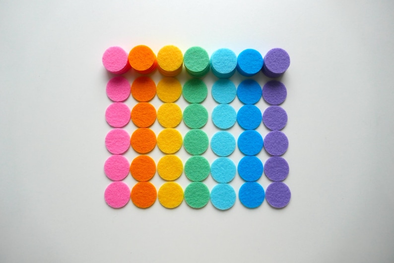 Może przedstawiać: Tęczowe filcowe k&oacute;łka ułożone w rzędach, z kolorami przechodzącymi od r&oacute;żowego do fioletowego.