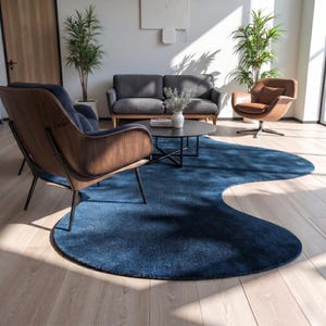 May include: A large, irregular, deep blue area rug with a soft, textured surface. The rug features a fluid, organic shape that curves across the light-coloured wooden floor, providing a bold contrast to the surrounding furniture and decor.