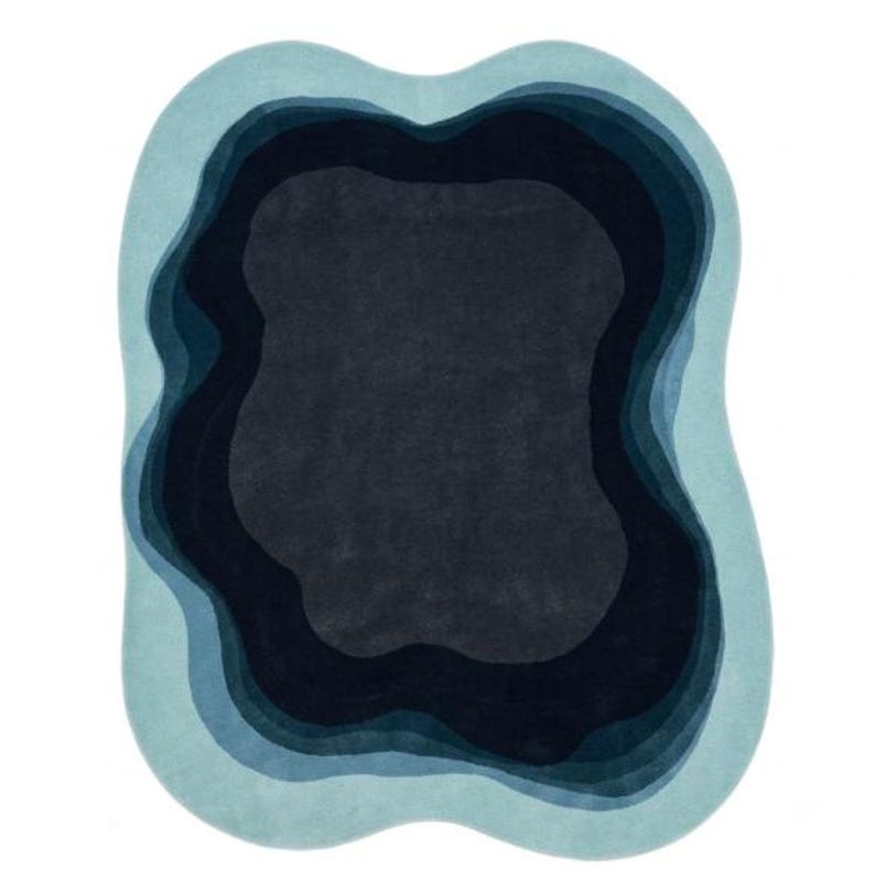 May include: An area rug with an irregular, organic shape featuring concentric, wavy layers of colour. The design transitions from a dark charcoal centre through shades of navy and medium blue, ending with a light aqua border on the outer edge.