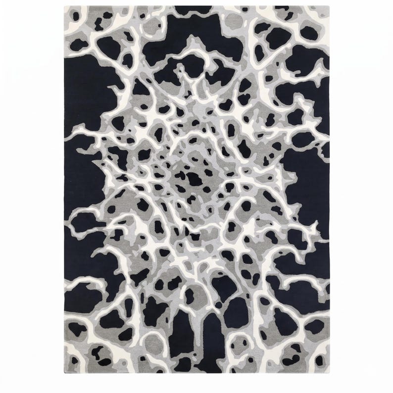 Puede incluir: Una alfombra rectangular con un patr&oacute;n abstracto de alto contraste en negro, blanco y varios tonos de gris. El dise&ntilde;o consiste en formas org&aacute;nicas interconectadas que irradian desde el centro, creando un efecto visual complejo y estratificado.
