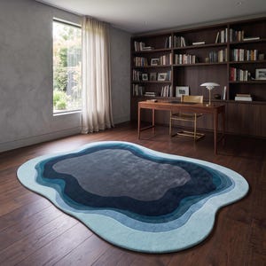 May include: An irregular, organic-shaped area rug featuring concentric layers of blue, ranging from light sky blue at the outer edge to deep navy and dark charcoal grey in the centre, creating a topographical, layered effect on the floor.