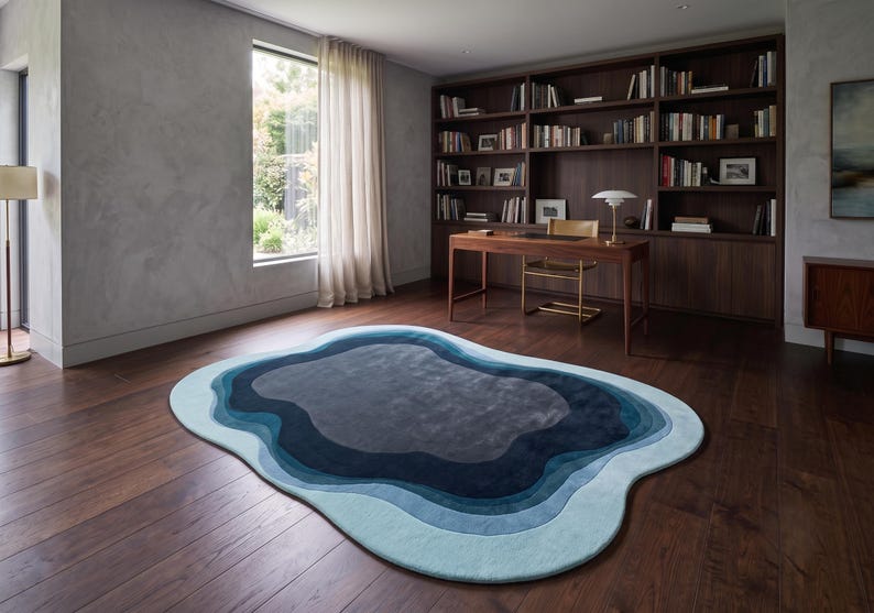May include: An irregular, organic-shaped area rug featuring concentric layers of blue, ranging from light sky blue at the outer edge to deep navy and dark charcoal grey in the centre, creating a topographical, layered effect on the floor.
