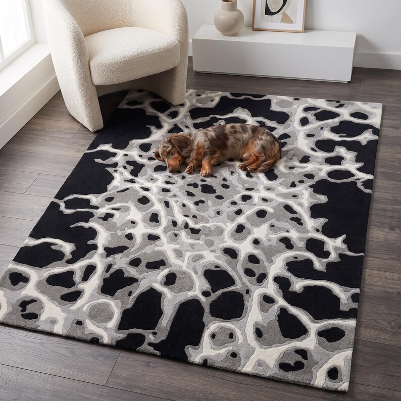 Puede incluir: Una alfombra rectangular con un patr&oacute;n org&aacute;nico y abstracto de formas interconectadas en negro, gris carb&oacute;n, gris claro y blanco roto. El dise&ntilde;o consiste en formas fluidas similares a amebas que crean un efecto visual de alto contraste.