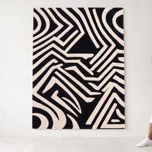 Puede incluir: Una gran pieza de arte mural rectangular con un patr&oacute;n gr&aacute;fico de alto contraste de l&iacute;neas gruesas entrelazadas en negro y crema. El dise&ntilde;o consiste en formas geom&eacute;tricas y caminos curvos que crean un efecto visual complejo y laber&iacute;ntico.