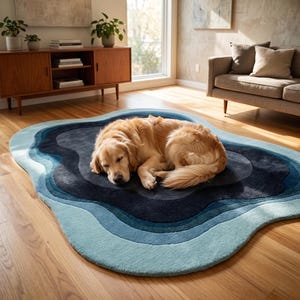 May include: An irregular, organic-shaped area rug featuring concentric, wavy layers of blue, ranging from light sky blue at the outer edges to a deep, dark navy blue in the centre, with a golden-coloured dog resting on the rug's surface.